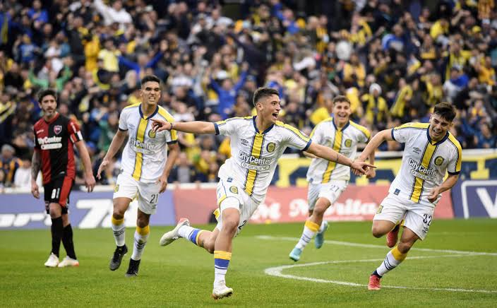 Jugador de Rosario Central festejando un gol con los brazos abiertos, con la camiseta alternativa blanca