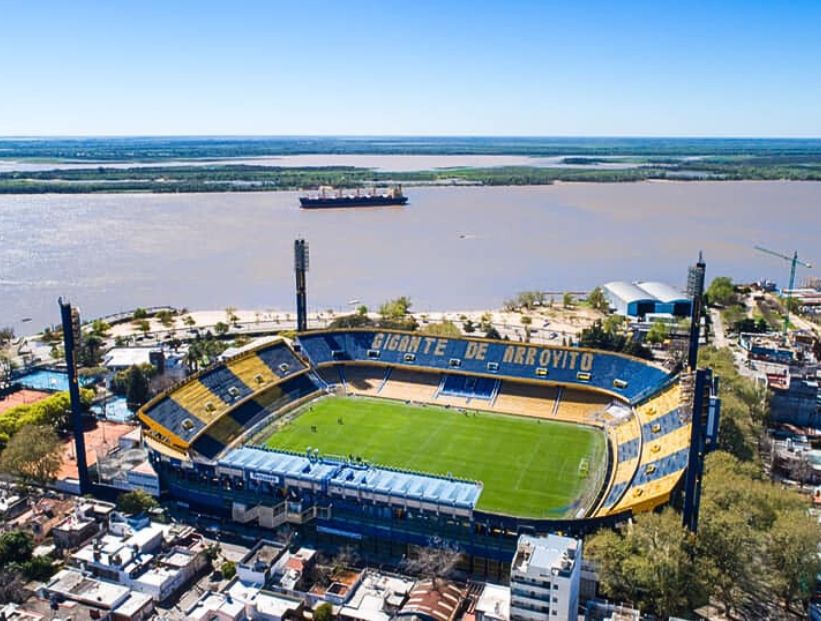 Vista aérea del Gigante de Arroyito junto al río Paraná, con un buque de carga pasando frente al estadio